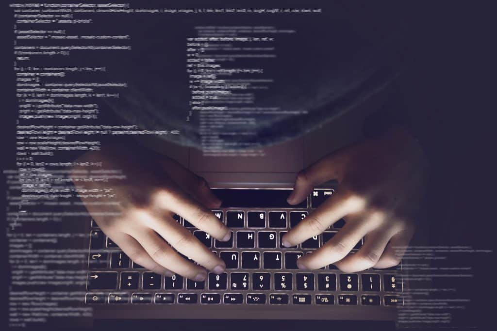 Symbolbild Cybersecurity - Hände auf einer Computertastatur, im Hintergrund: verschwommene Codezeilen