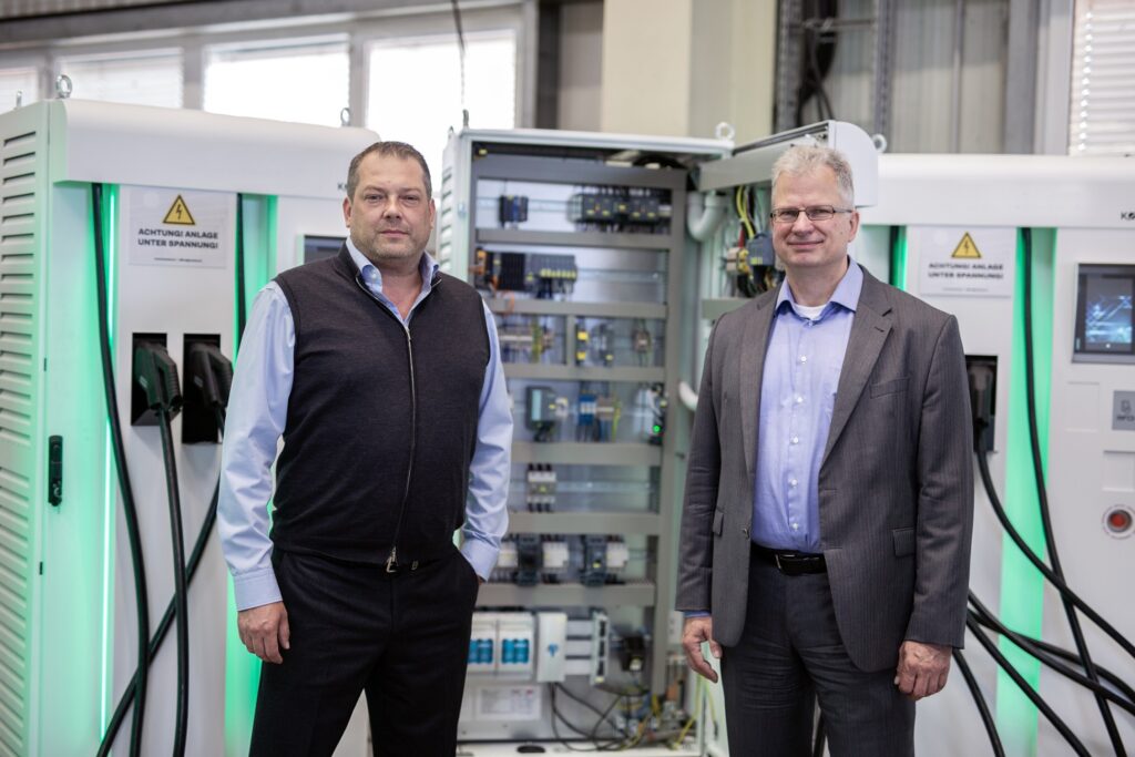 CEO Kostad und Michael Freyny von Siemens stehen in einer Halle vor Ladestationen
