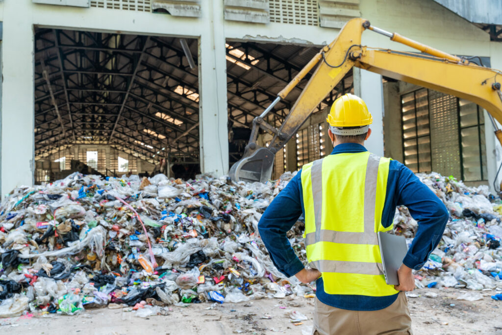 Recycling industry engineer monitoring loader machine performance surrounded by stacks of recyclable materials at waste separation plant.
